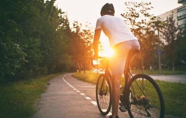 Young man in casual clothes cycling on a bike path in an urban area as the sun sets